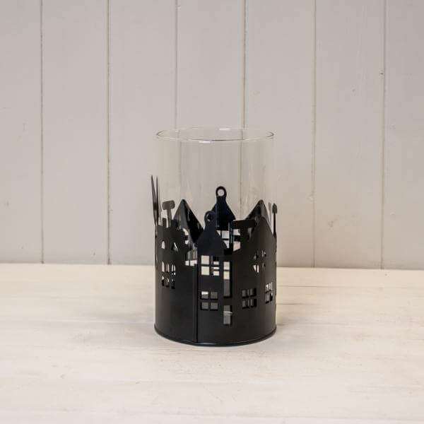 Large Black Metal House Scene Candle Holder with Glass Insert on a white wooden surface.