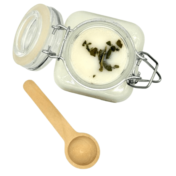 Aloha Scoopable Wax Melt in a glass jar with a wooden scoop, featuring botanical herbs on top.