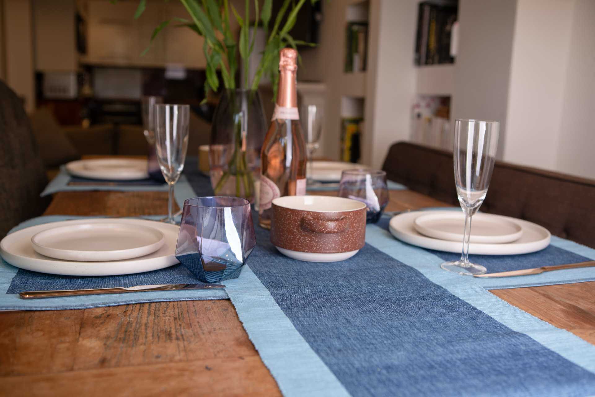 Luxury Placemats Blue - 4 Pack set on a dining table with plates, glassware, and a bottle of champagne.