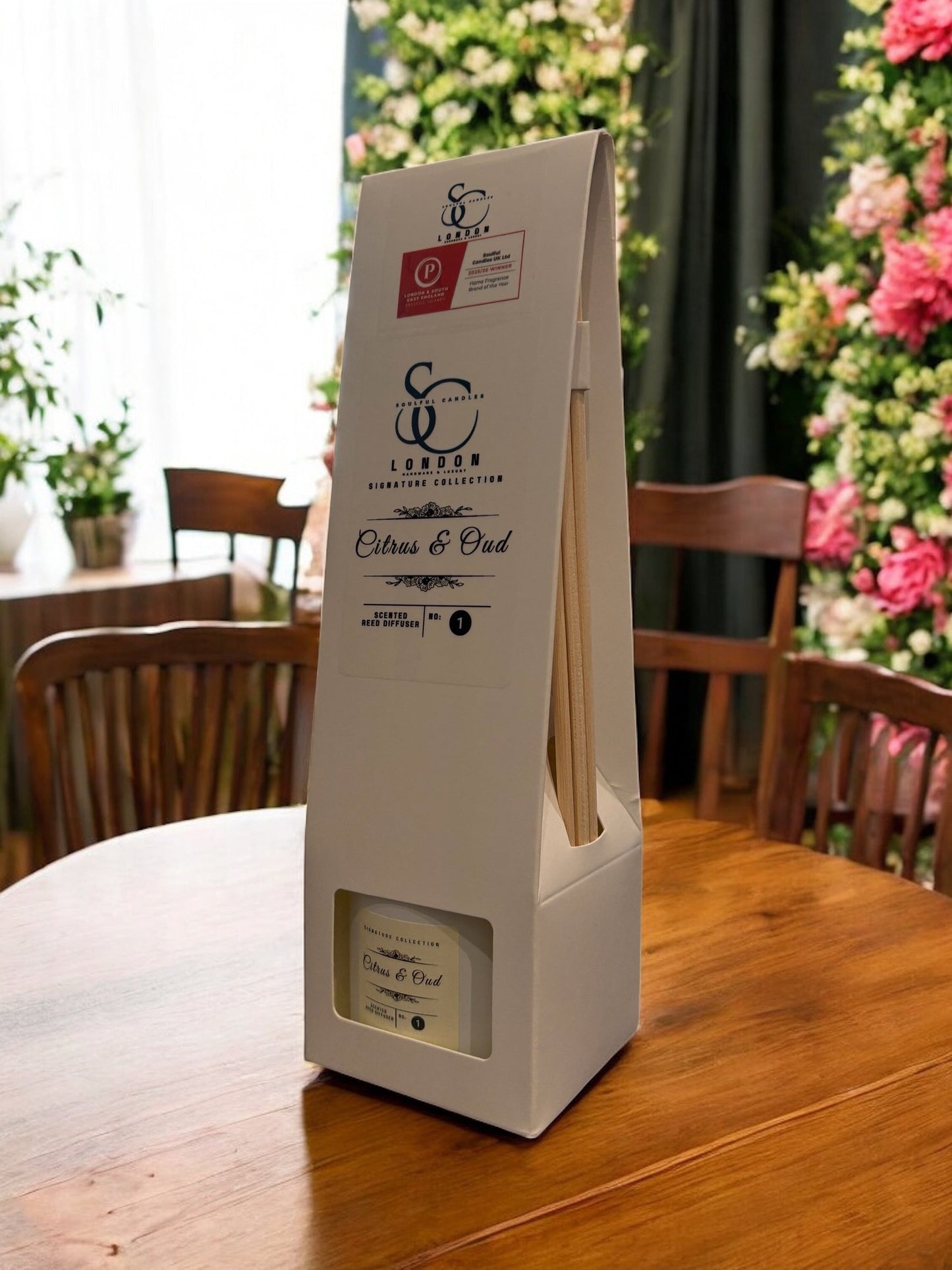 Citrus & Oud Reed Diffuser 100ml displayed on a wooden table with floral backdrop.