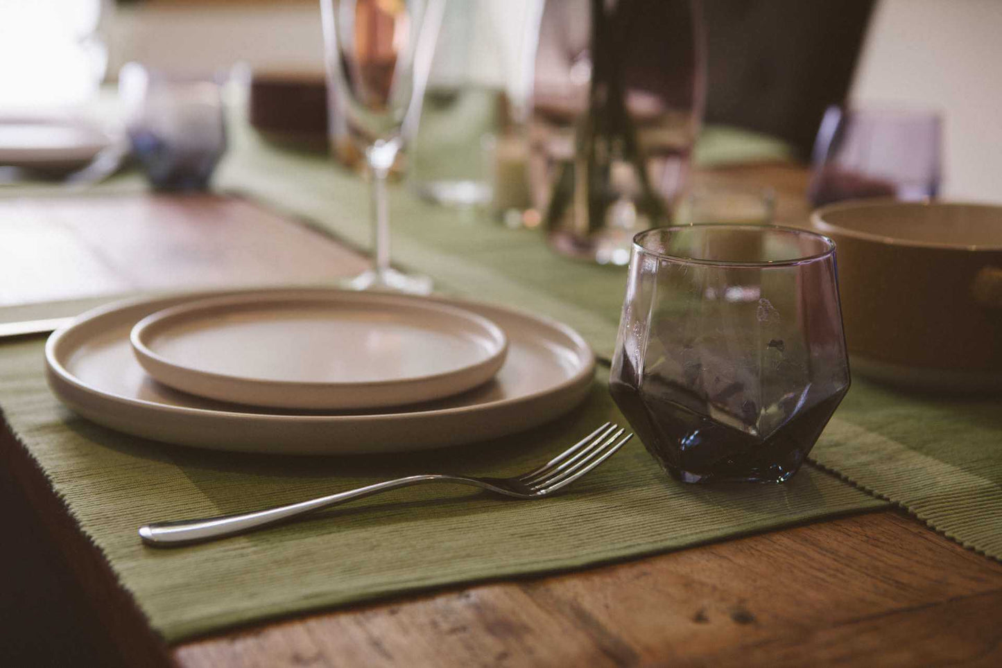 Luxury Placemats Green - 4 Pack displayed on a wooden dining table with plates and a glass.