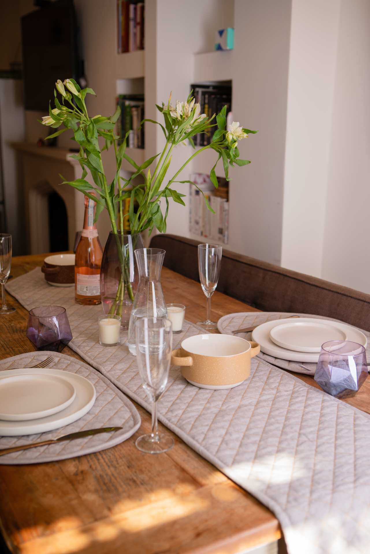 Quilted Table Runner - Organic Cotton on a dining table with dishes, glasses, and flowers.
