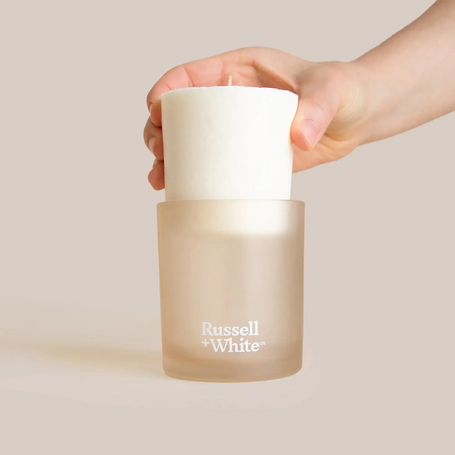 Hand holding a frosted glass candle holder with a white candle inside, featuring Russell + White branding.
