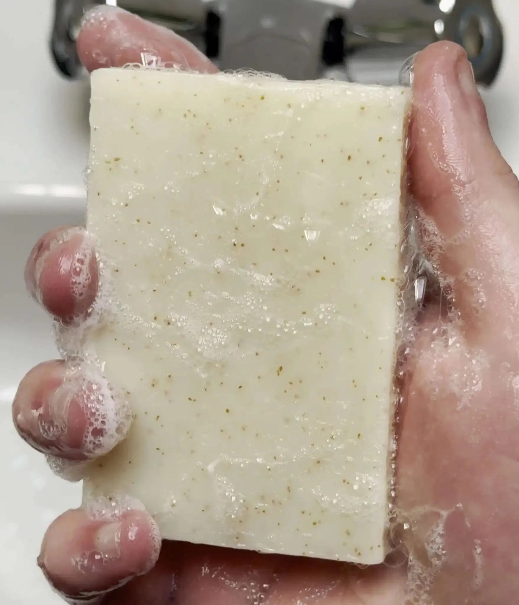 Eucalyptus Lemon Mint and Olive Stone Natural Soap Bar held in a hand with bubbles, showing its natural texture and refreshing qualities.