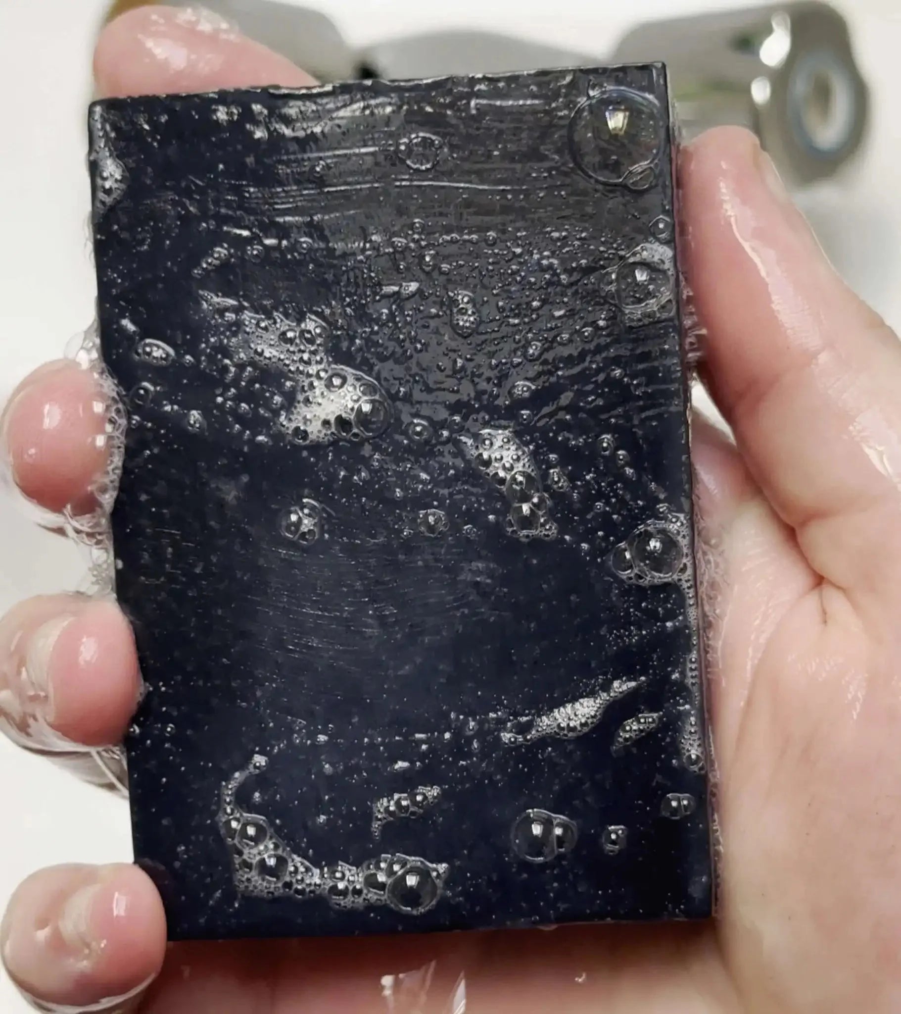 Lime & Charcoal Natural Soap Bar being used with bubbles in a hand under running water.