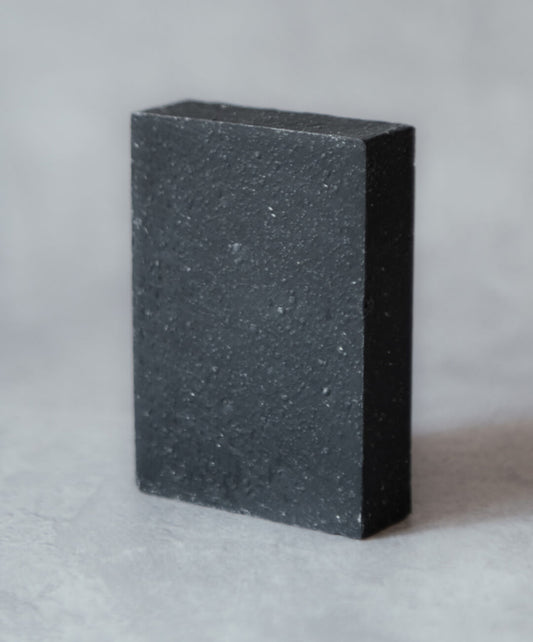 Lime & Charcoal Natural Soap Bar on a textured surface, highlighting its unique charcoal color and texture.