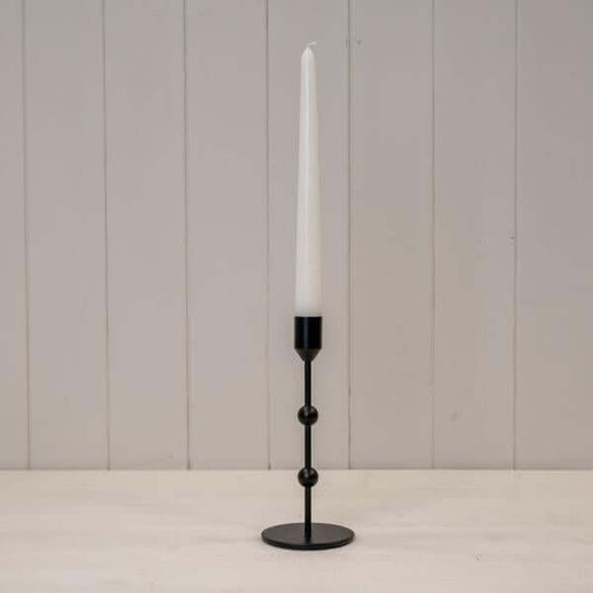 Medium Black Single Metal Candle Stick with a tall white candle on a wooden table.