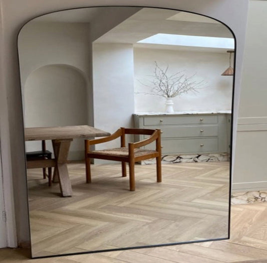 Yoko - Black Metal Gentle Arch Mirror - 120cm x 95cm reflecting a stylish interior with wooden chair and cabinet.