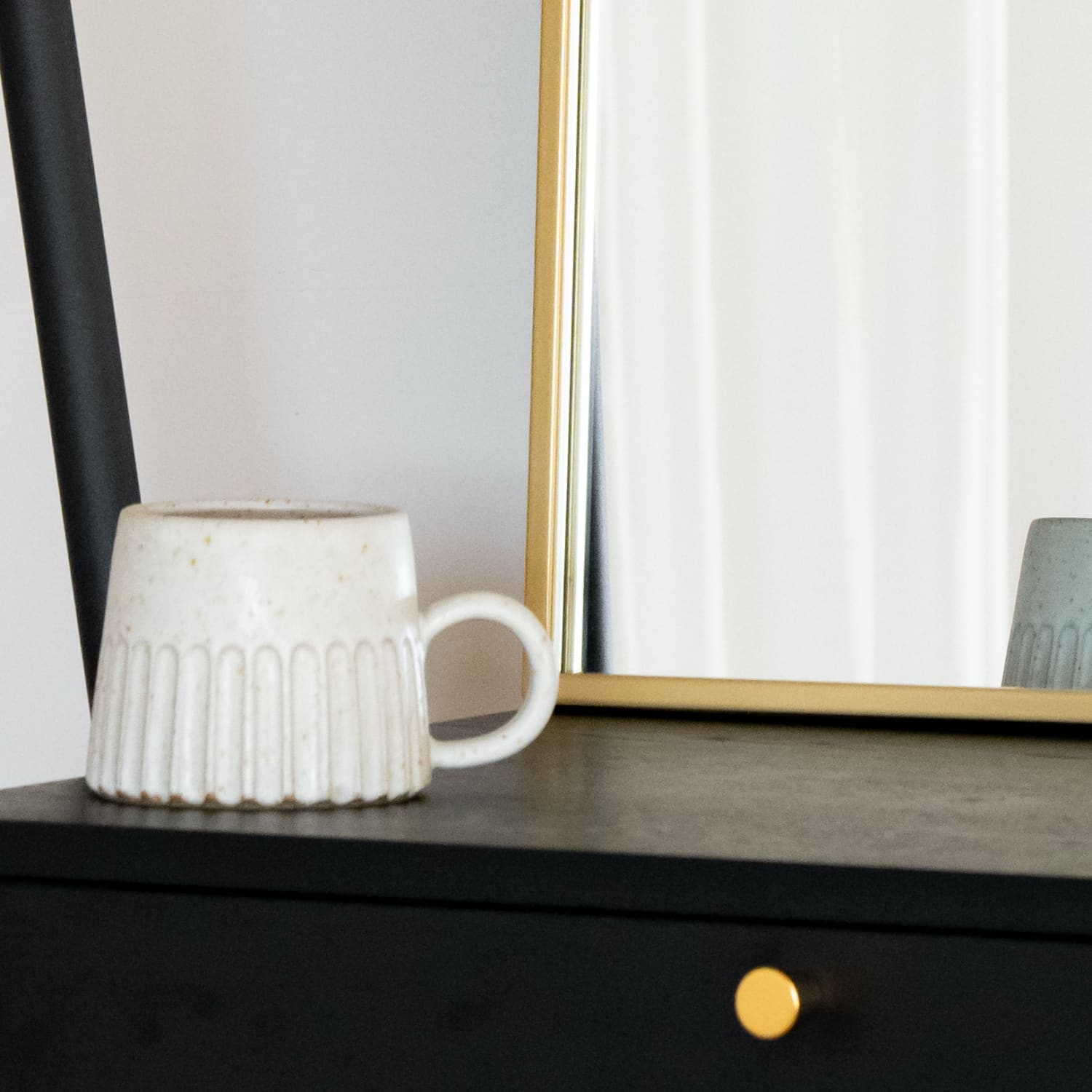Yoko - Gold Metal Gentle Arch Mirror - 120cm x 95cm reflected behind a modern ceramic mug.